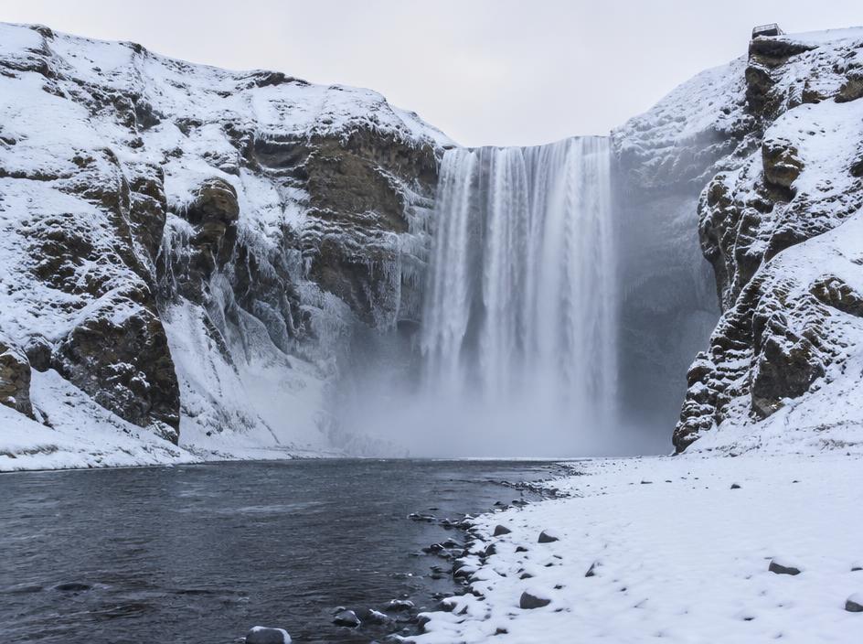 Skógafoss Waterfall pouring between snow-dusted cliffs in winter