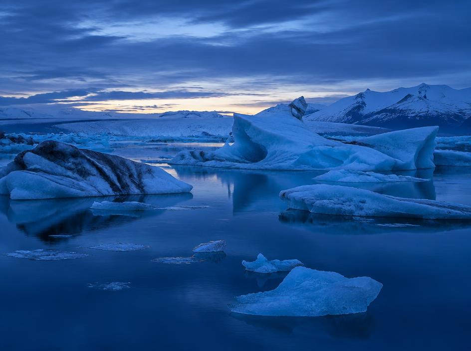 Blue icebergs floating in Jökulsárlón Glacier Lagoon at blue hour beneath snowy peaks