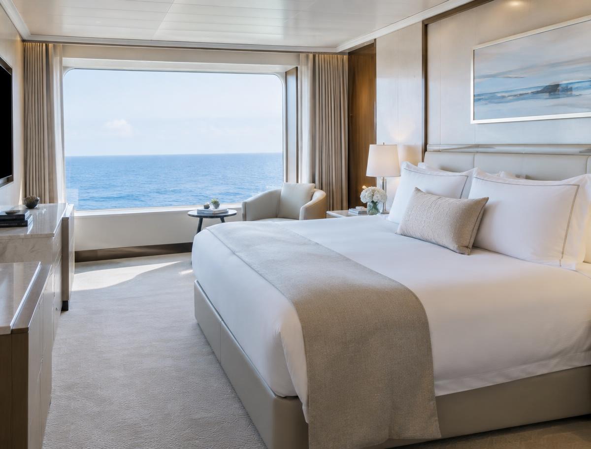 A bright ship suite with crisp white linens and a wide window onto the open sea